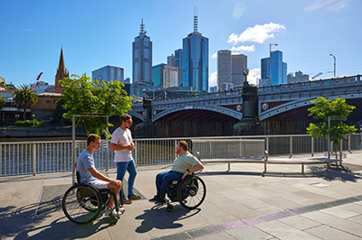 Three people next to the Yarra River, two in wheelchairs and one standing