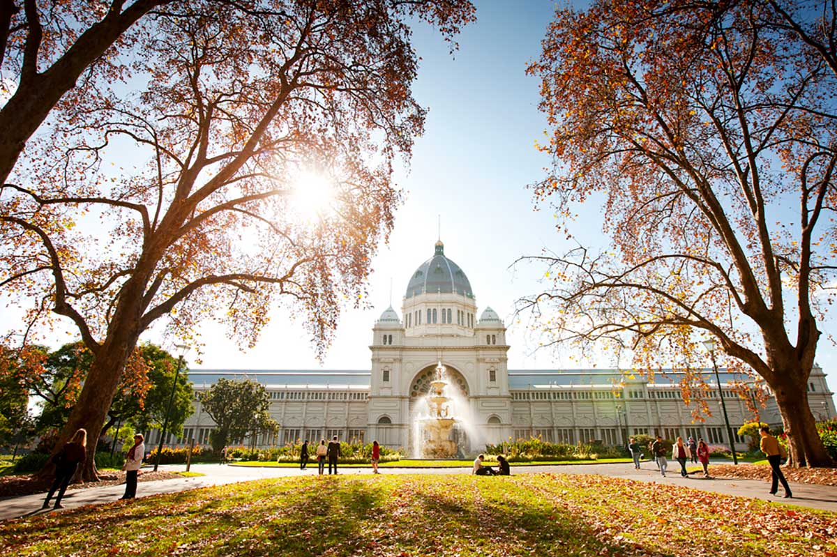 The Royal Exhibition Building in Carlton Gardens with a decorative water fountain in front, and framed by large trees in the foreground.