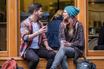 Two people sitting outside drinking from reusable coffee cups