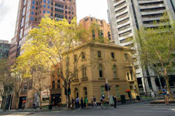 Heritage building on city street corner with high-rise buildings on either side