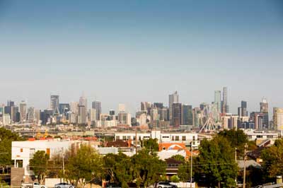Melbourne city skyline in the distance with trees and low-rise buildings in the foreground