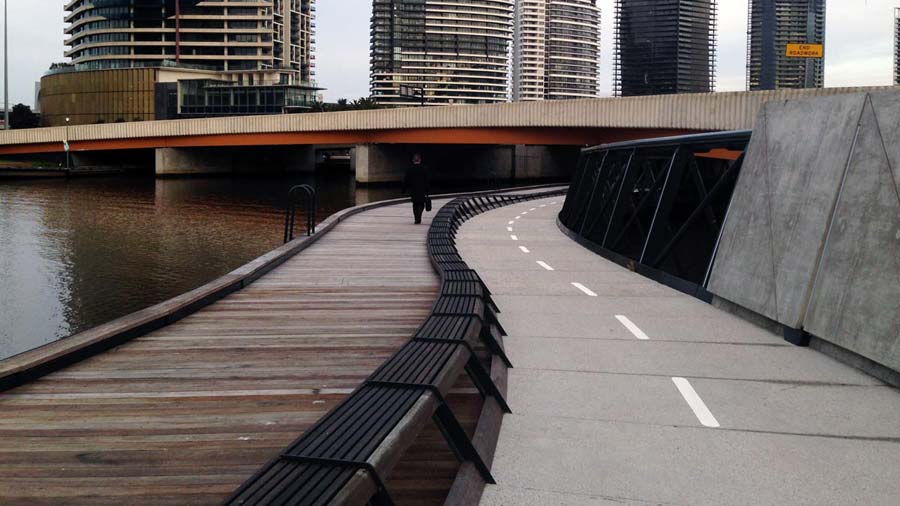 Jim Stynes Bridge showing the path and boardwalk curving beneath a road bridge and floating alongside the river