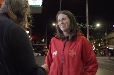 A person wearing a bright red jacket with a city of Melbourne and Salvation army logo on it.