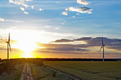 Two wind turbines with a dramatic sunset sky in the background