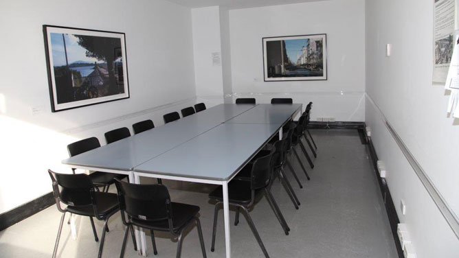 A room with white walls and table in the middle with 16 chairs