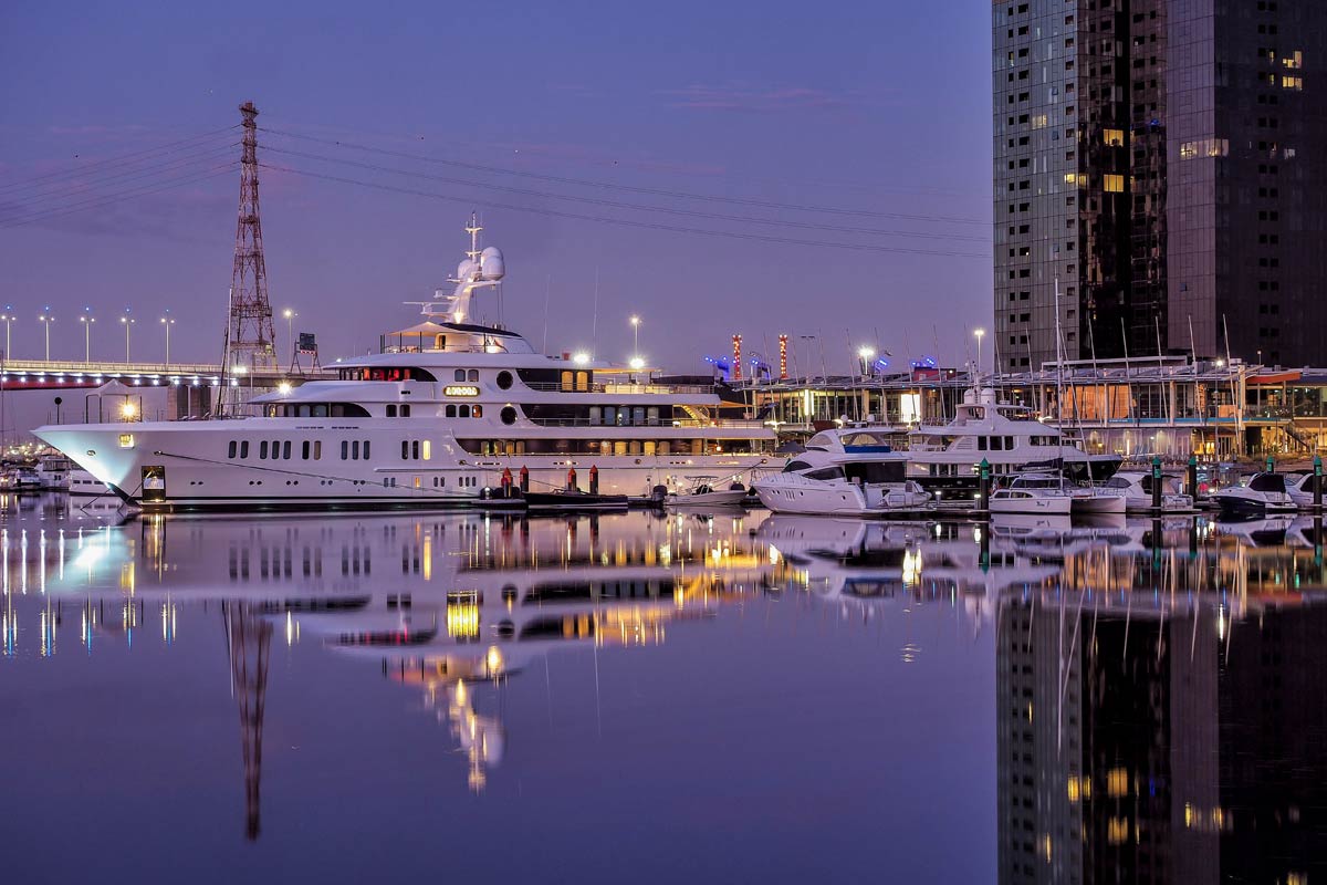 A superyacht and smaller boats reflected in the water at dusk