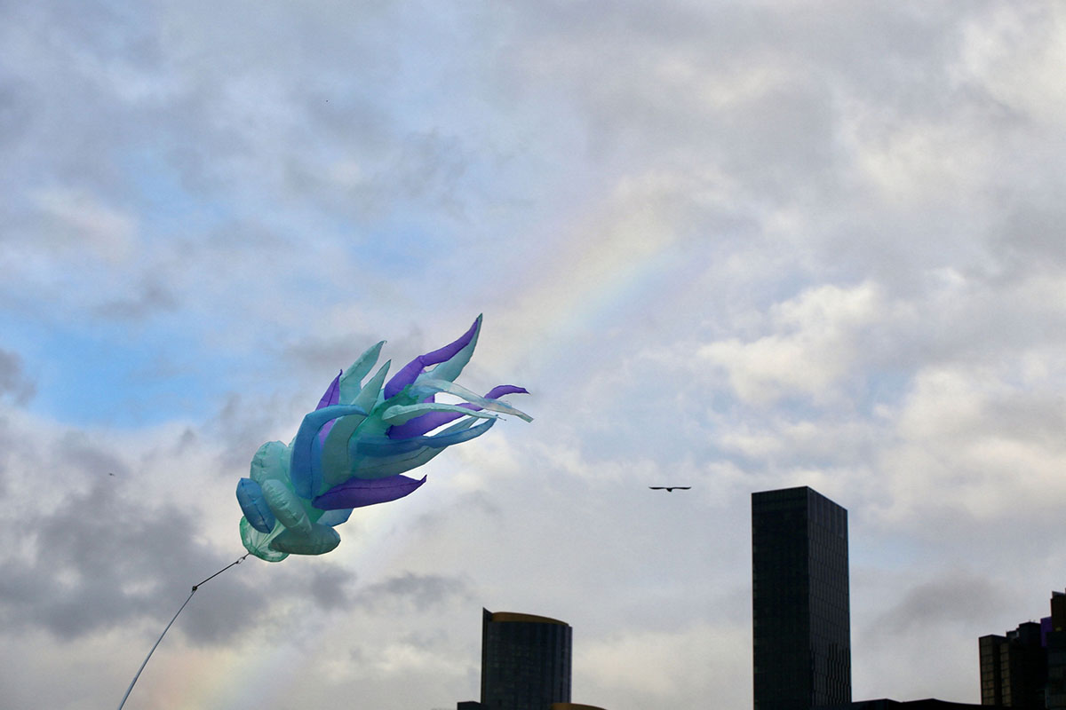 Flying sculpture with rainbow over city skyline