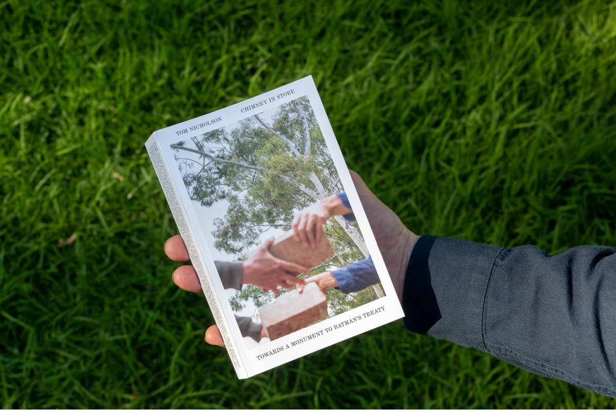 A human hand holding a book in front of grass.