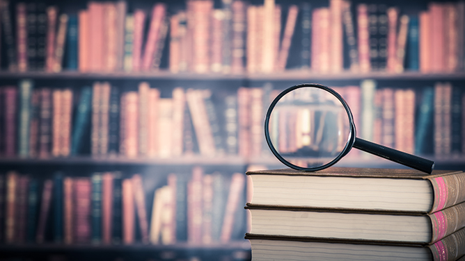A magnifying glass sitting on a pile of books in front of a full book shelf